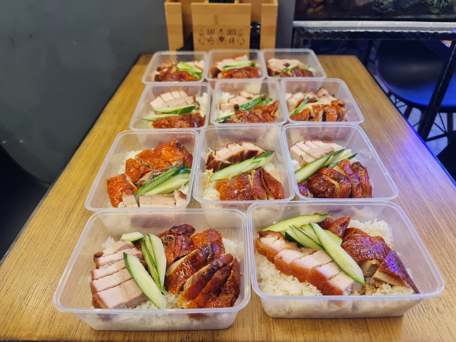 A dozen rice boxes of roast meats packed on the counter for collection.